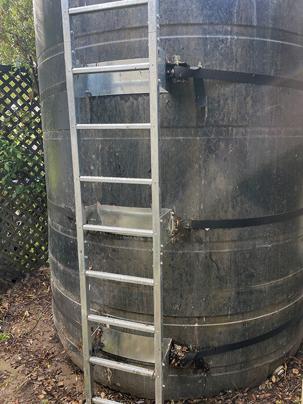 Poly water tank with a ladder on a grassy area