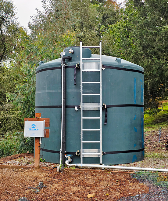 Large blue water storage tank with a ladder in a natural setting